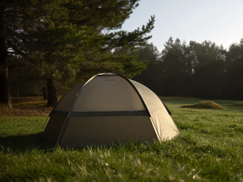 Kleines Kuppelzelt in der Morgendämmerung auf einer Wiese am Waldrand, Tau im Gras