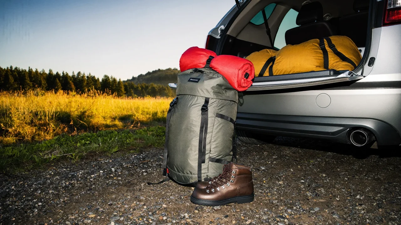 Gepackter Rucksack, Wanderstiefel und Schlafsack neben einem Kofferraum bei Sonnenaufgang